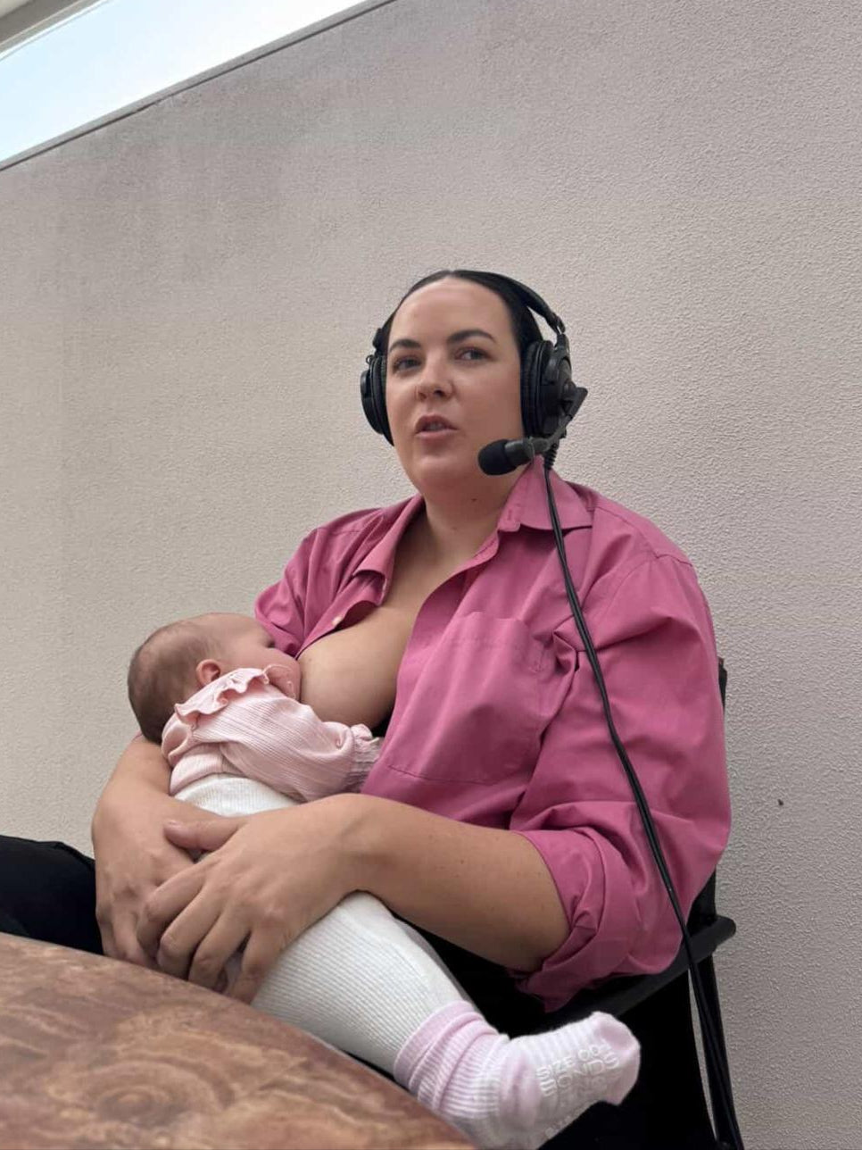 Woman in pink shirt holding a baby in a room with a window.